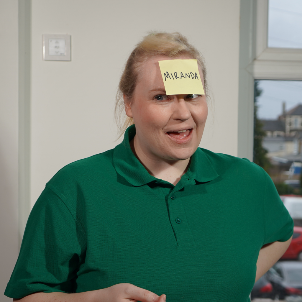A woman in a green shirt leading a workshop - she has a sticker that read's 'Miranda' on her forehead